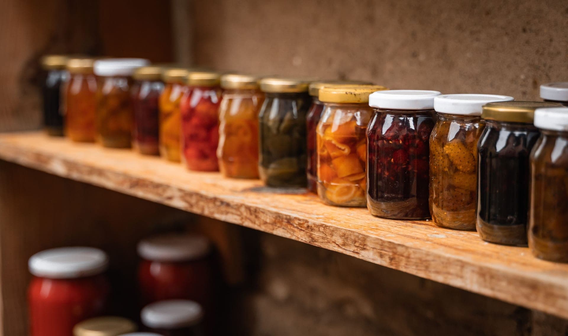 Home-preserved fruit and vegetables in sealed mason jars on a dark wooden shelf