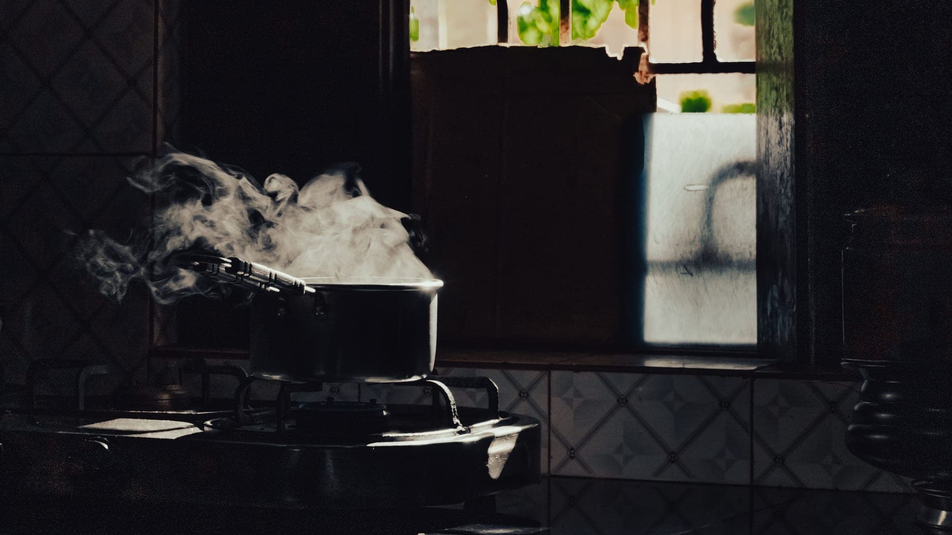Steam rising from a large pot on a stove in a dark kitchen